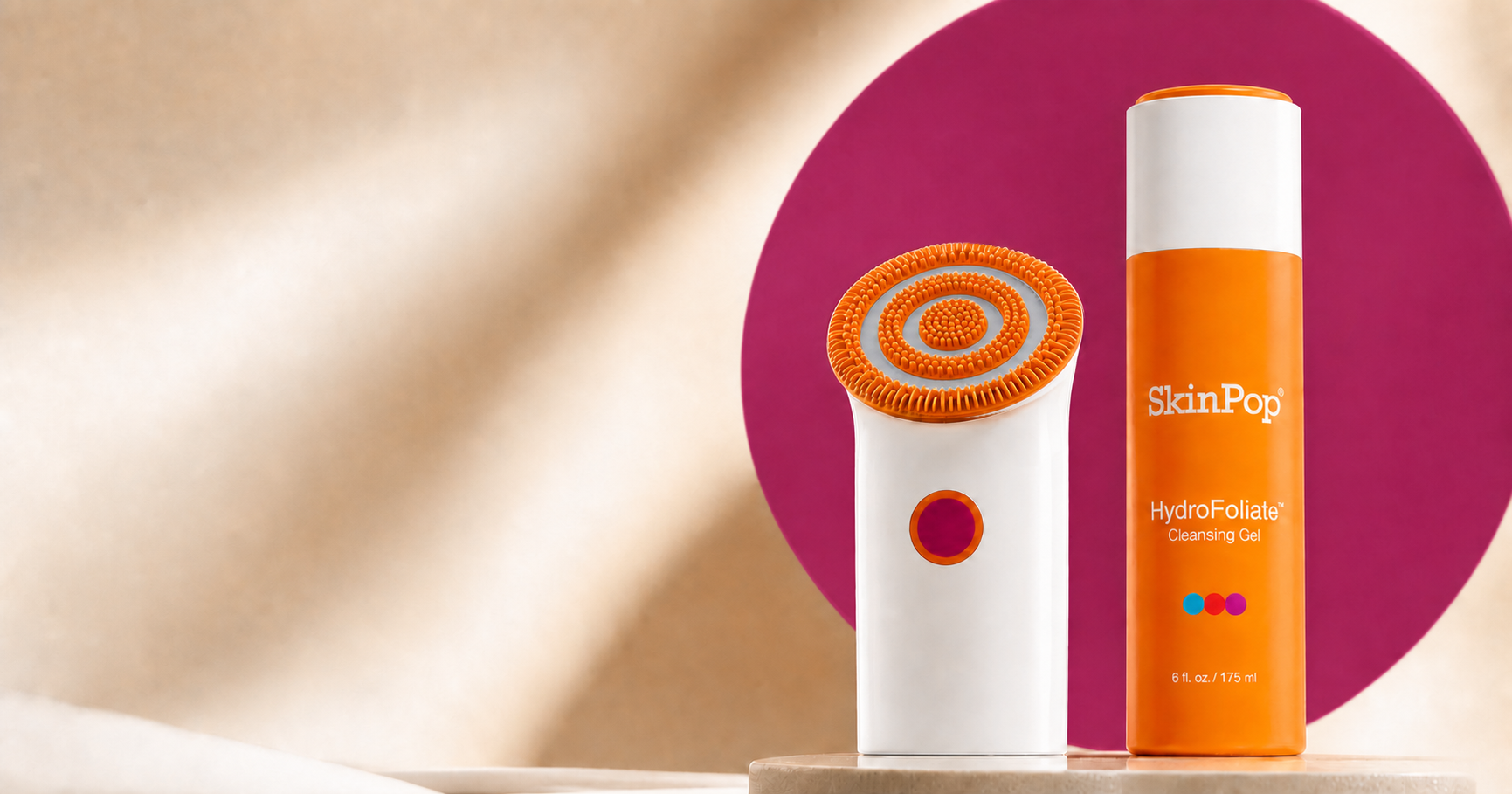 White SkinPop device and closed orange HydroFoliate gel in a warm sculptural studio setting with a raspberry-purple backdrop