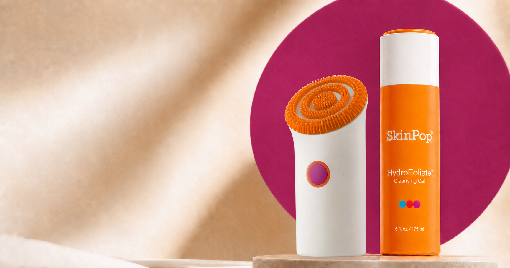 White SkinPop device and closed orange HydroFoliate gel in a warm sculptural studio setting with a raspberry-purple backdrop